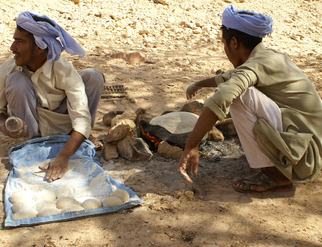 Two Bedouin men sitting on the ground, skillfully making traditional bread