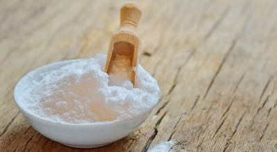 A bowl of baking soda with a wooden spoon resting on top, ready for use in baking or cooking