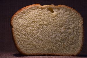 A slice of sandwich bread displayed on a brown background, highlighting its texture and color